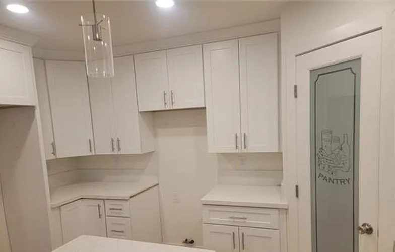 Gabinetes de cocina blancos junto a una puerta de despensa con vidrio esmerilado
