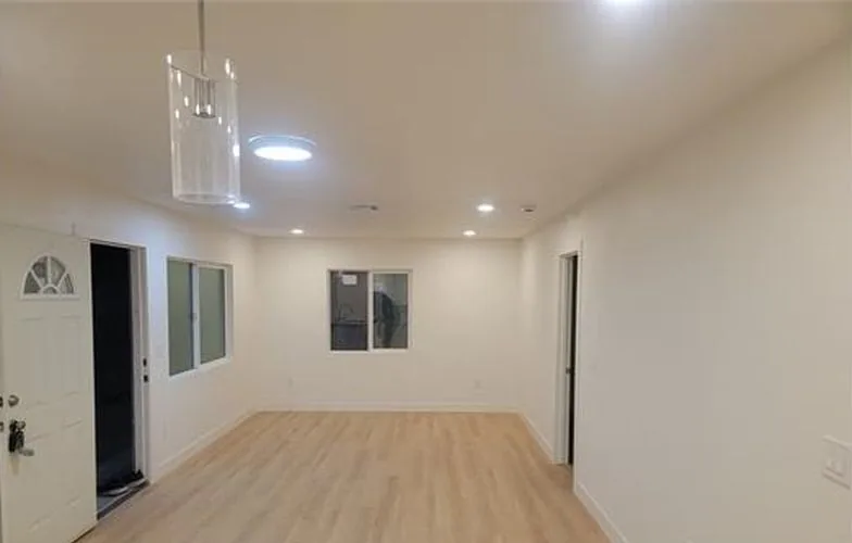 Sala abierta con piso tipo madera y una puerta principal con ventana en arco