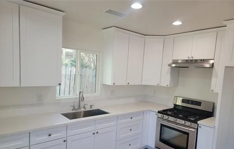Cocina con gabinetes blancos, estufa de gas y una ventana sobre el fregadero