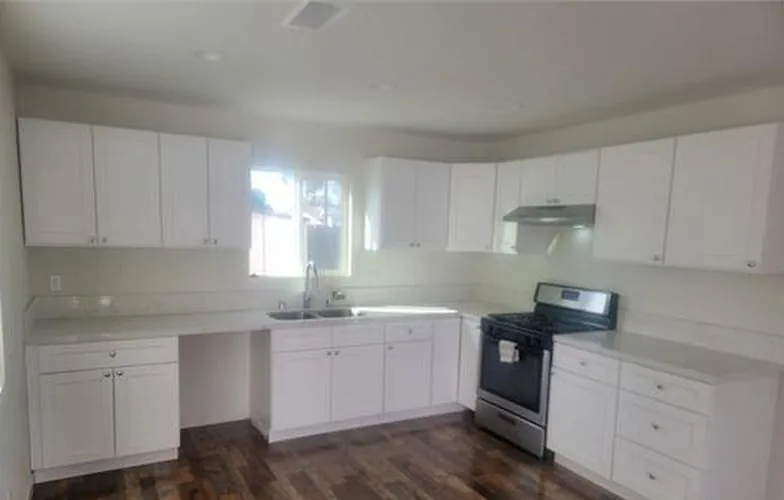 Cocina en L con gabinetes blancos, estufa de acero inoxidable y piso oscuro tipo madera