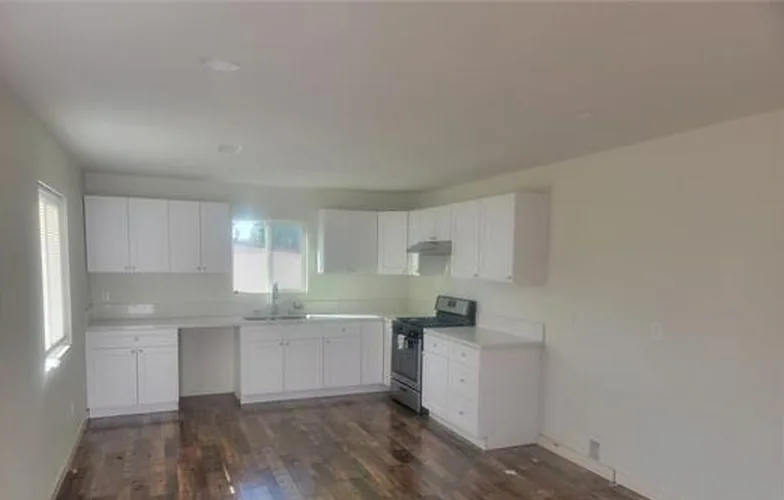 Vista amplia de una cocina blanca y piso oscuro tipo madera