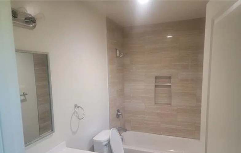 Baño con regadera de azulejo alrededor de la tina, un nicho y un lavabo blanco